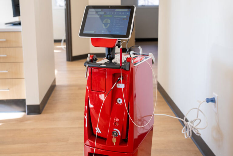 Red dental soft tissue laser machine with touchscreen interface in a modern clinic hallway, used for precise and minimally invasive dental procedures.