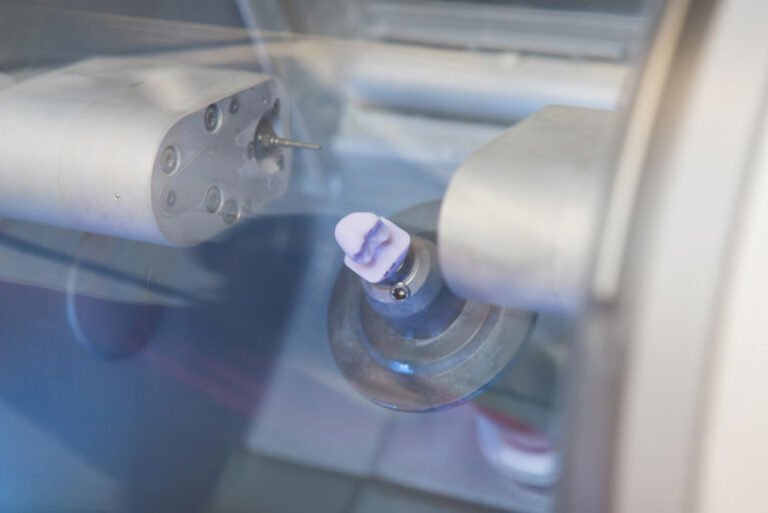 Close-up of a dental milling machine crafting a ceramic crown using CAD/CAM technology.
